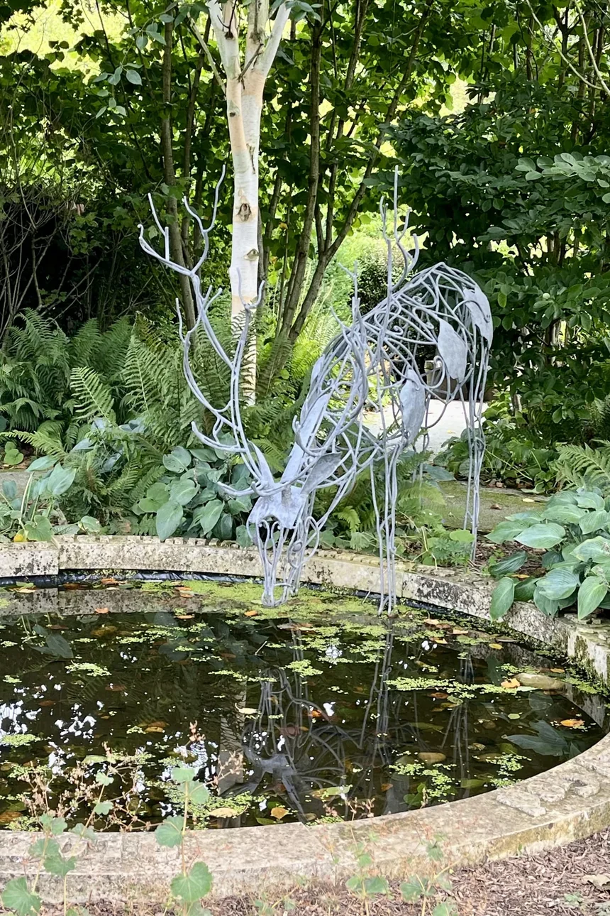 A wire stag sculpture standing in a garden pond