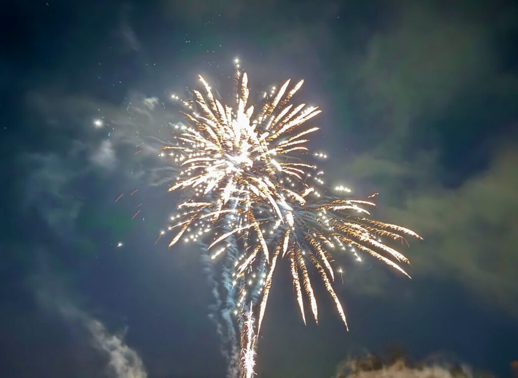 A golden firework bursting against a cloudy night sky