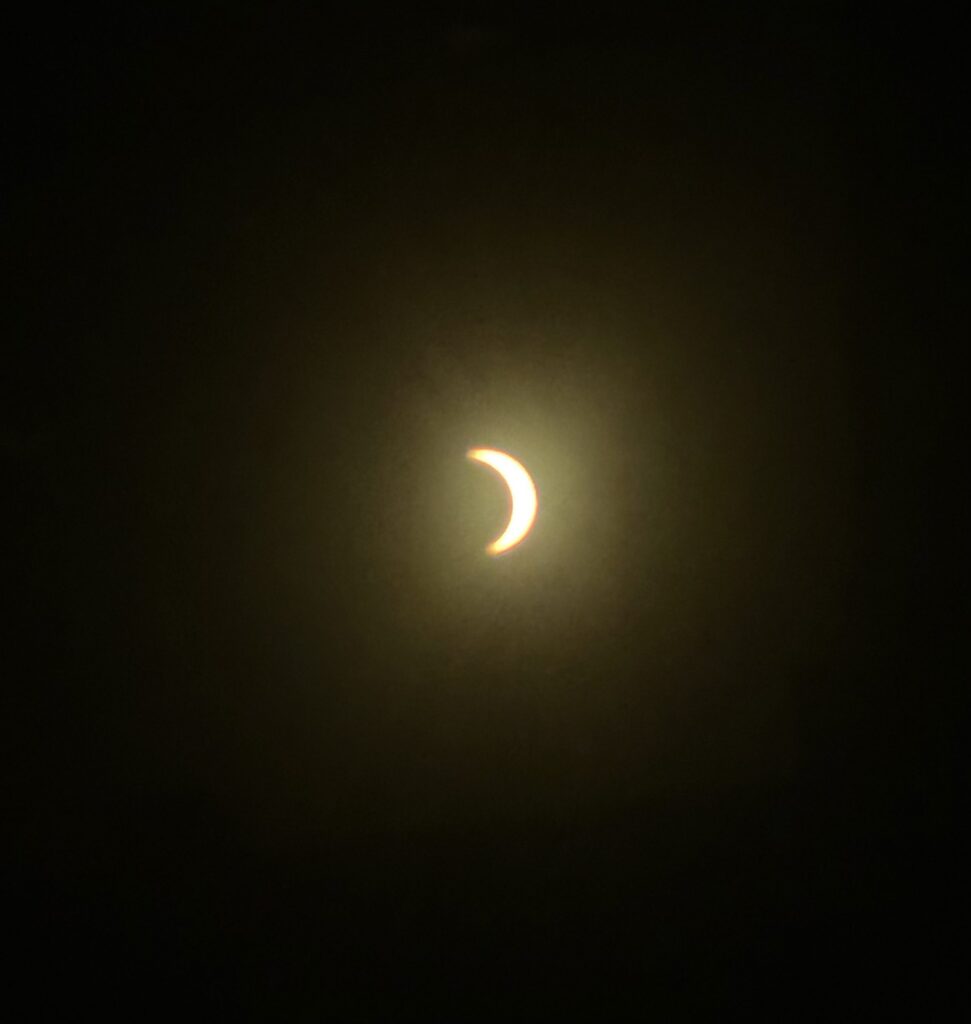 A thin bright crescent of the sun against a dark sky during the partial solar eclipse