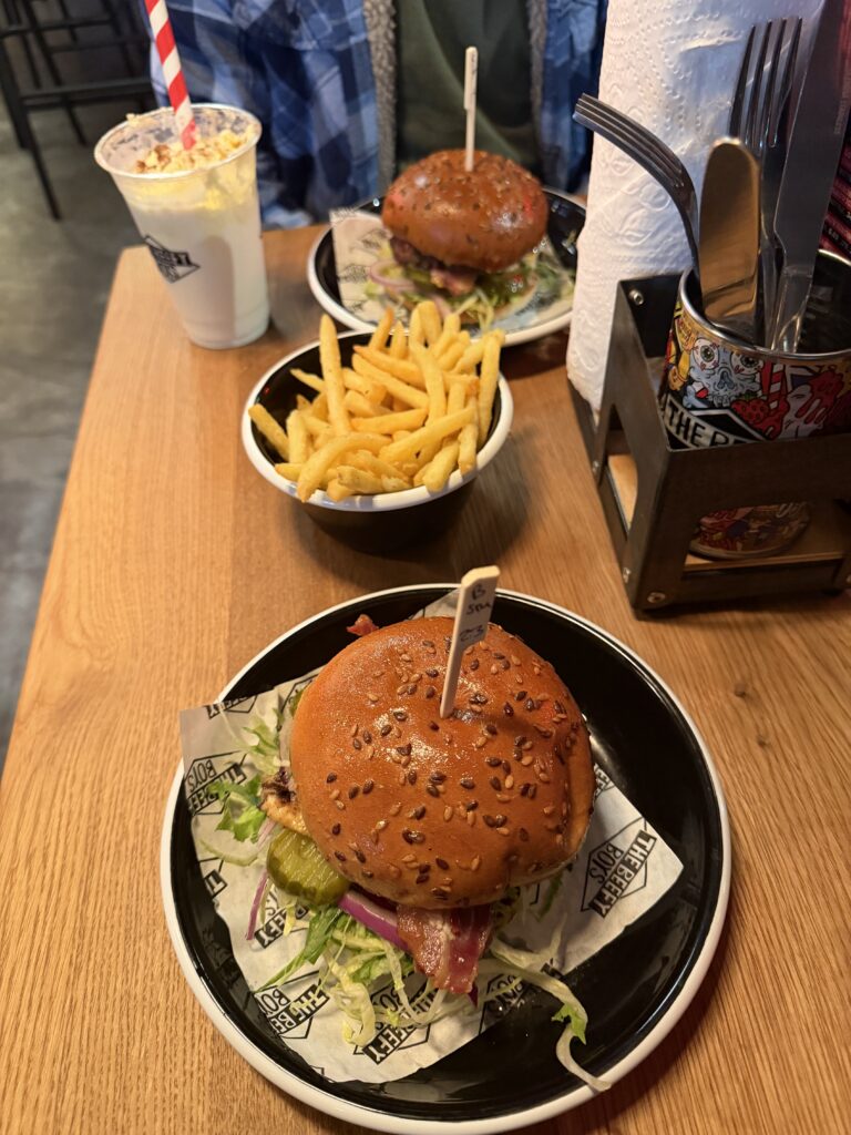 Two bacon burgers in sesame brioche buns on black plates, with a bowl of fries and a milkshake, at The Beefy Boys in Exeter